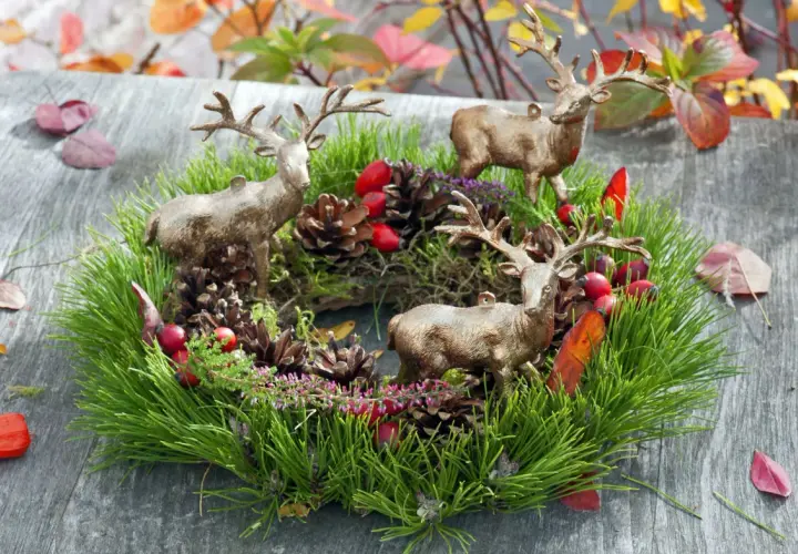 Drei Hirschfiguren schmücken einen grünen Kranz mit Tannenzweigen, Zapfen und roten Beeren. Tolle Herbstkranz Ideen für Ihr Zuhause.