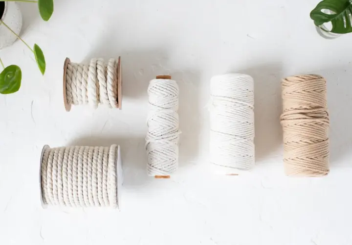 Verschiedene Garne für Makramee: dicke und dünne Schnüre in Weiß und Beige, aufgewickelt auf Spulen und Rollen.