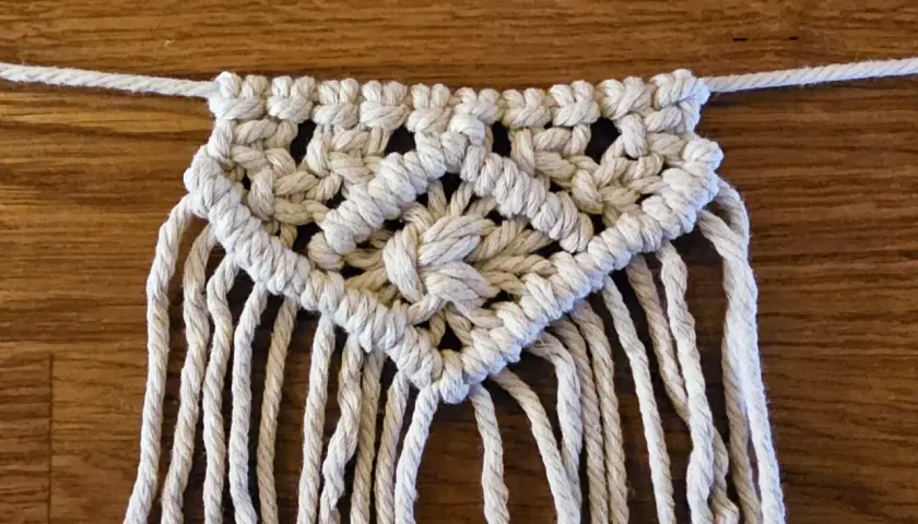 Detailaufnahme einer Makramee-Wimpelkette mit Anleitung. Die Kette ist aus weißer Schnur geknüpft und zeigt ein komplexes Muster.