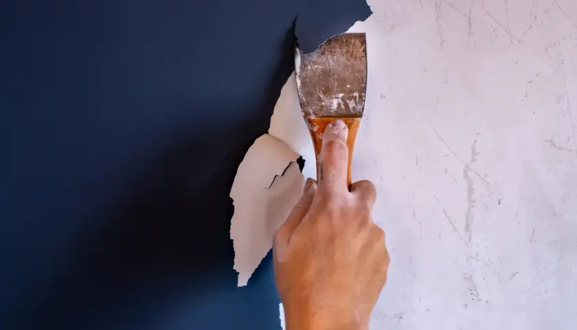 Hand schabt mit einem Spachtel die alte Farbe ab. Der Prozess, Farbe entfernen, beginnt.