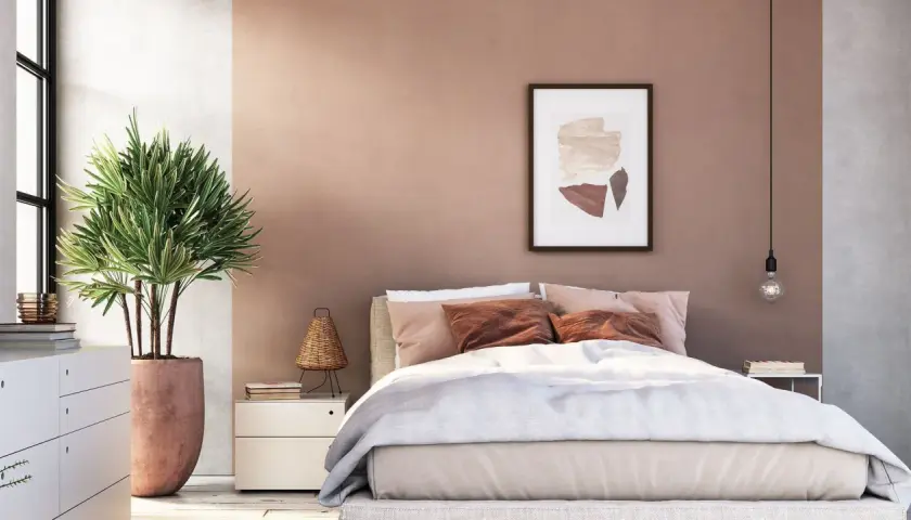 Gemütliches Schlafzimmer mit warmen Wandgestaltung Farben in Rosé- und Erdtönen. Ein Bett mit beiger Bettwäsche und braunen Kissen lädt zum Entspannen ein.