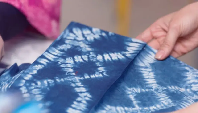 Hände falten ein tiefblaues Tuch mit dem Muster der Shibori Technik.
