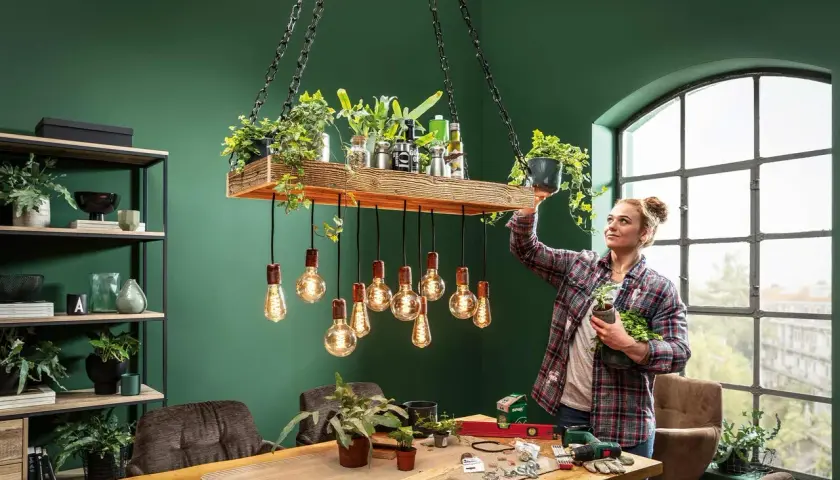 Frau dekoriert eine selbstgemachte Lampe mit Pflanzen. Ein DIY-Projekt für ein grünes Zuhause.
