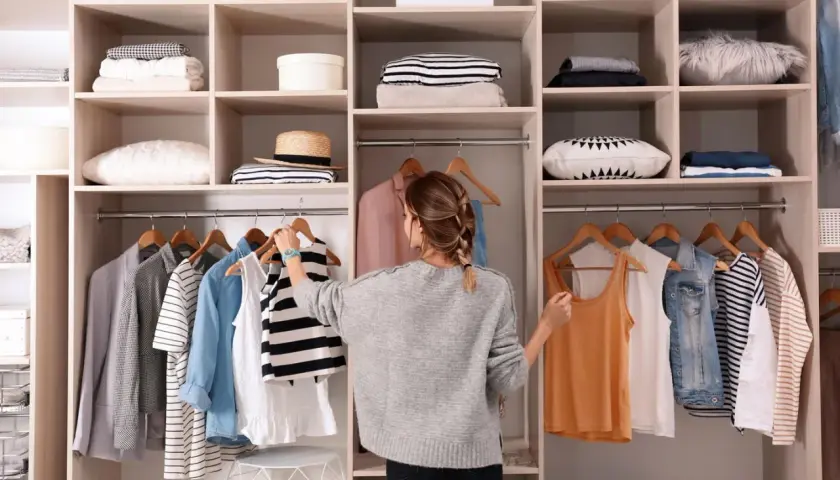 Frau sortiert Kleidung im offenen Kleiderschrank. Hier sind clevere Kleiderschrank Aufteilung Tipps für Ordnung.