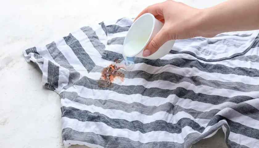 Flüssigkeit wird auf einen Fleck auf einem gestreiften T-Shirt gegossen, um Wandfarbe aus Kleidung zu entfernen.