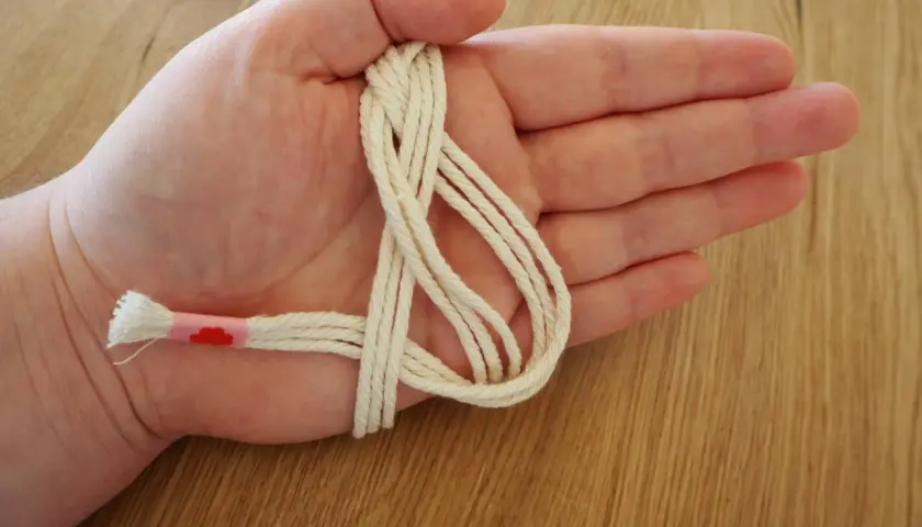 Hand hält cremefarbene Schnur für makramee serviettenringe anleitung. Ein Teil ist mit rosa Band umwickelt.