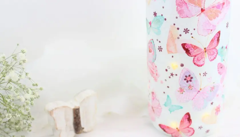 Zauberhaftes Basteln mit Servietten: Ein Glas mit bunten Schmetterlingen, kleine Lichter und eine Holzschmetterling-Deko.