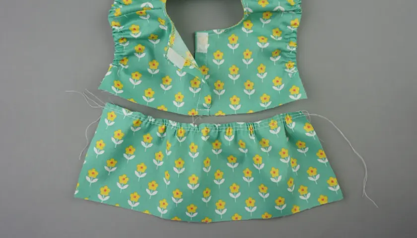 Zwei Teile eines **Puppenkleid Schnittmusters** mit Blumenmuster: Oberteil mit Rüschen und Klettverschluss, Rockteil mit Gummizug.