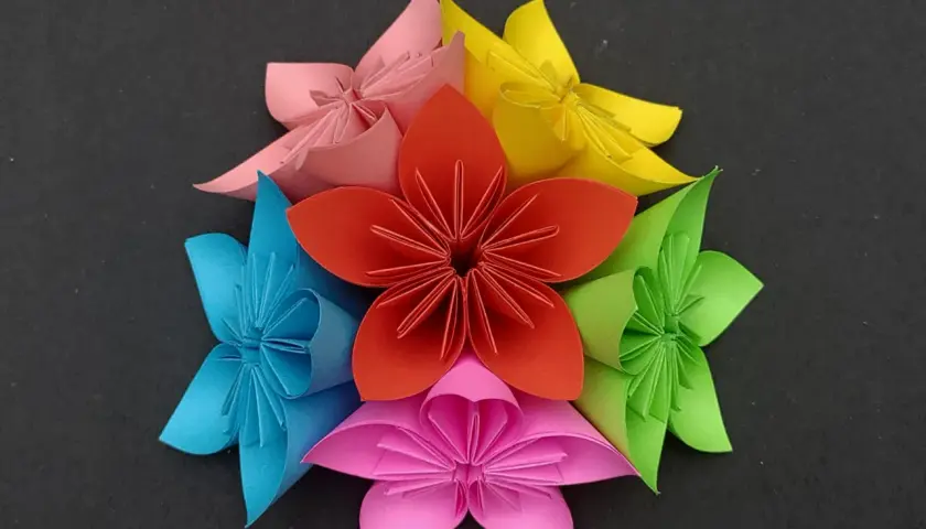 Bunte origami blumen arrangiert in einem Kreis auf schwarzem Hintergrund.