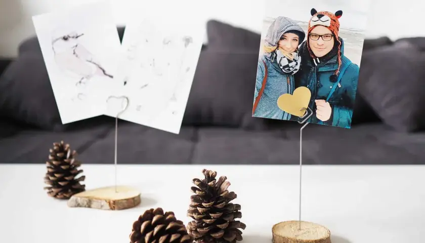 Selbstgemachte Fotohalter aus Holzscheiben und Draht mit Fotos von einem Paar und einem Vogel. Perfekt, um Erinnerungen zu präsentieren.