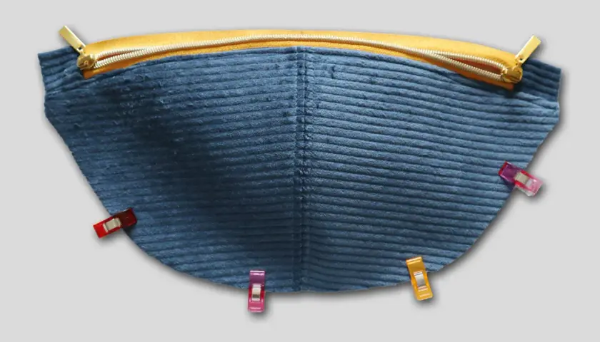 Blauer Cordstoff mit Reißverschluss und Nähklammern, bereit für das Schnittmuster einer Bauchtasche.