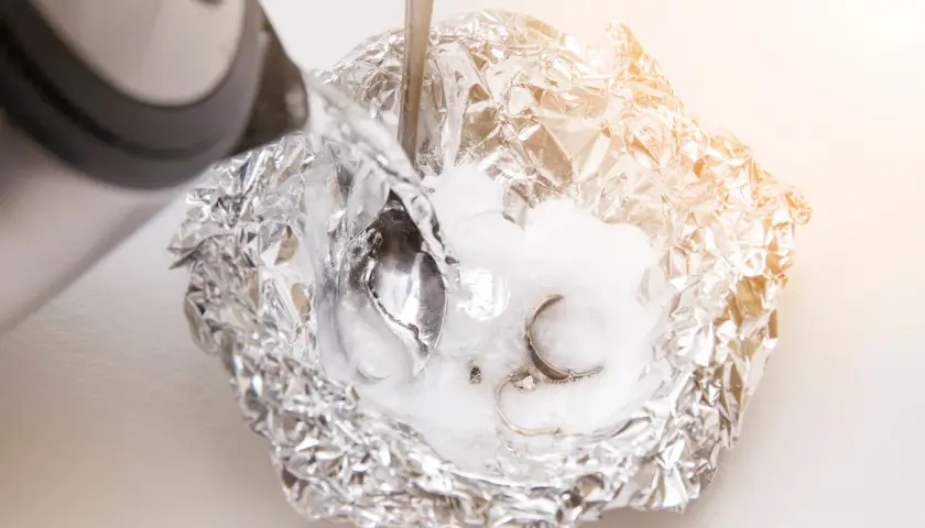 Silber putzen mit Natron: Heißes Wasser wird über Aluminiumfolie mit Natron und Schmuck gegossen, um angelaufenes Silber zu reinigen.