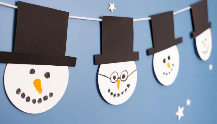 Schneemann-Girlande als winter bastelideen kinder. Weiße Kreise mit schwarzen Hüten und Gesichtern hängen an einer Schnur.