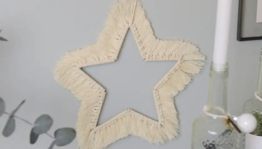 Ein Makramee Stern an der Wand, der wie eine Anleitung zum Nachbasteln aussieht.