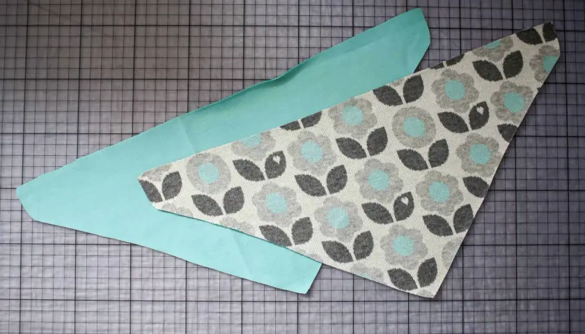 Zwei Stoffteile liegen auf einer Schneidematte. Ein Teil ist mintgrün, das andere hat ein Blumenmuster. Ein Schnittmuster für ein Halstuch Baby.
