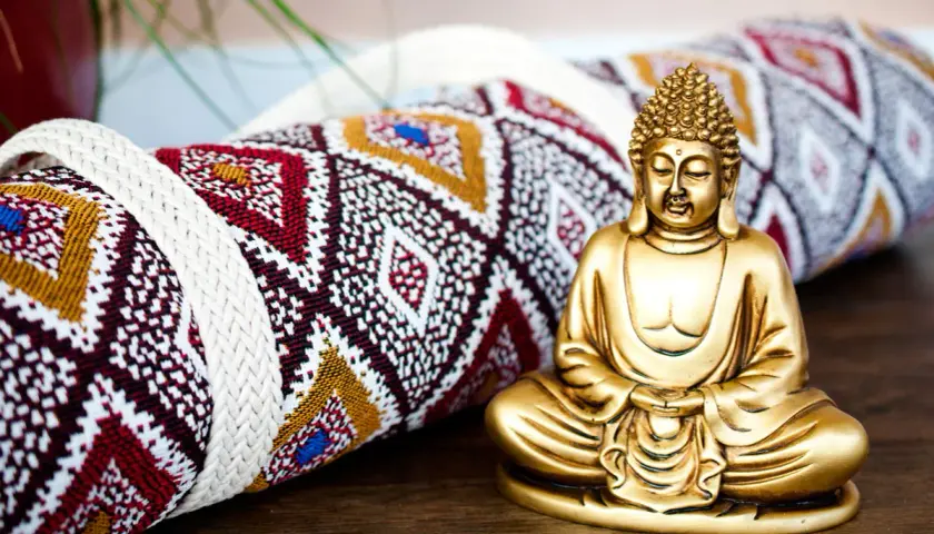 Goldene Buddha-Figur neben einer gerollten Yogamatte mit ethnischem Muster. Vielleicht das Schnittmuster für eine Yogatasche?