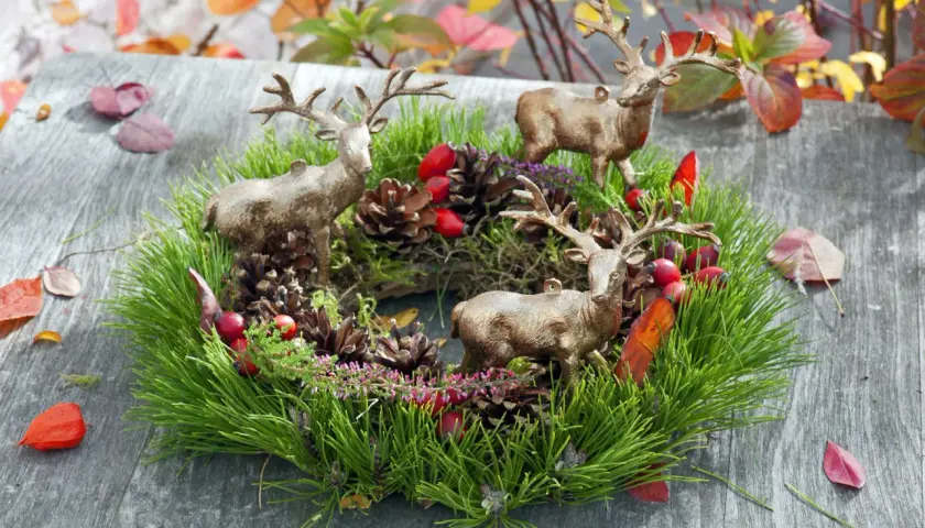 Drei Hirschfiguren schmücken einen grünen Kranz mit Tannenzweigen, Zapfen und roten Beeren. Tolle Herbstkranz Ideen für Ihr Zuhause.
