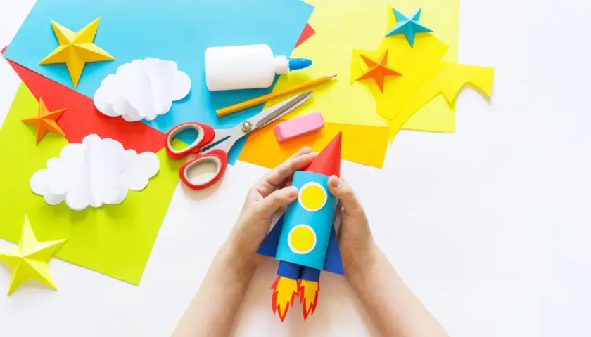 Kinder basteln einen Raketen-Weltraumflug. Alles für bastelkleber selber machen liegt bereit: Papier, Schere, Kleber, Stift.