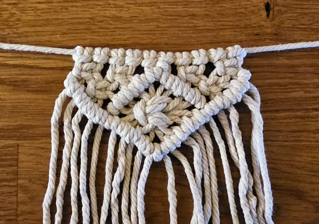 Detailaufnahme einer Makramee-Wimpelkette mit Anleitung. Die Kette ist aus weißer Schnur geknüpft und zeigt ein komplexes Muster.