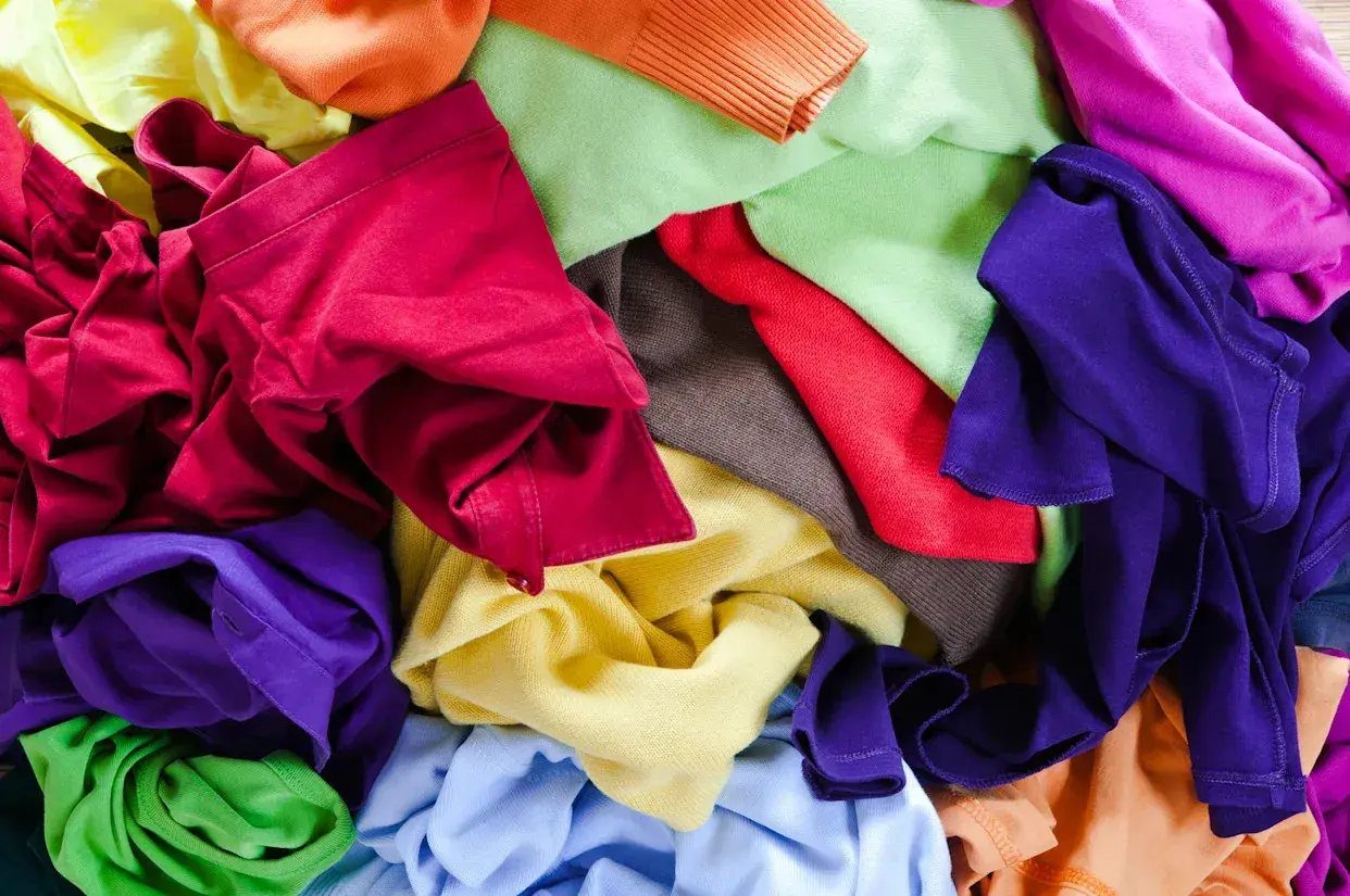 Bunte Stoffe, bereit für T-Shirt Upcycling. Ein Berg aus Rot, Lila, Grün, Gelb und Orange lädt zum kreativen Gestalten ein.