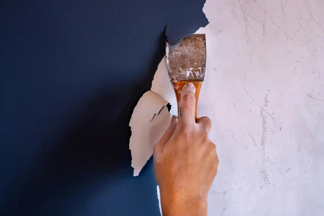 Hand schabt mit einem Spachtel die alte Farbe ab. Der Prozess, Farbe entfernen, beginnt.