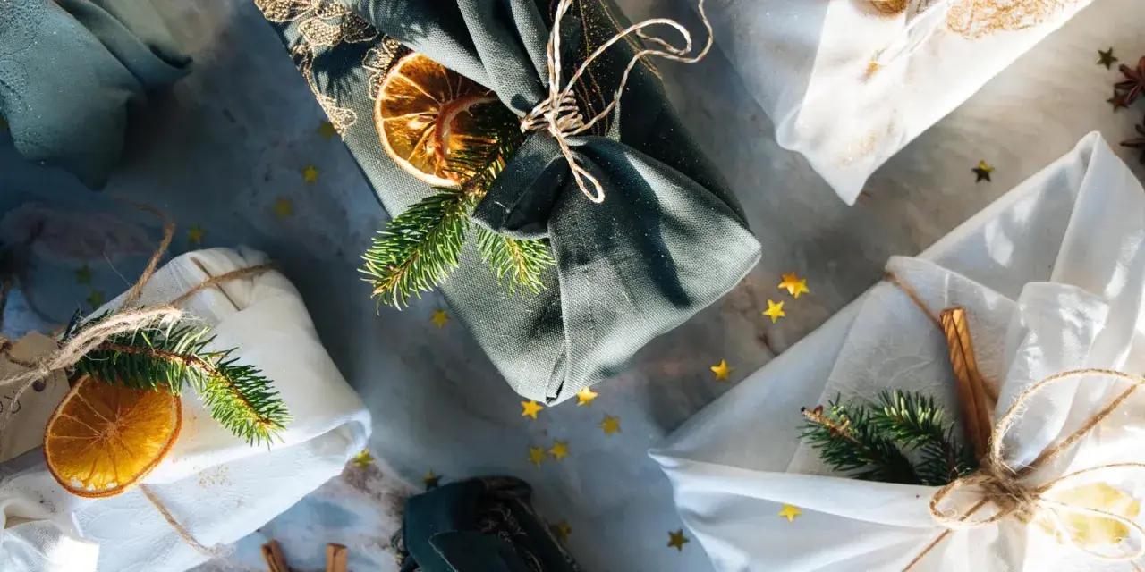 Geschenke liebevoll verpackt mit Stoff. Eine furoshiki anleitung für nachhaltige Geschenke, verziert mit Tannenzweigen und Orangenscheiben.