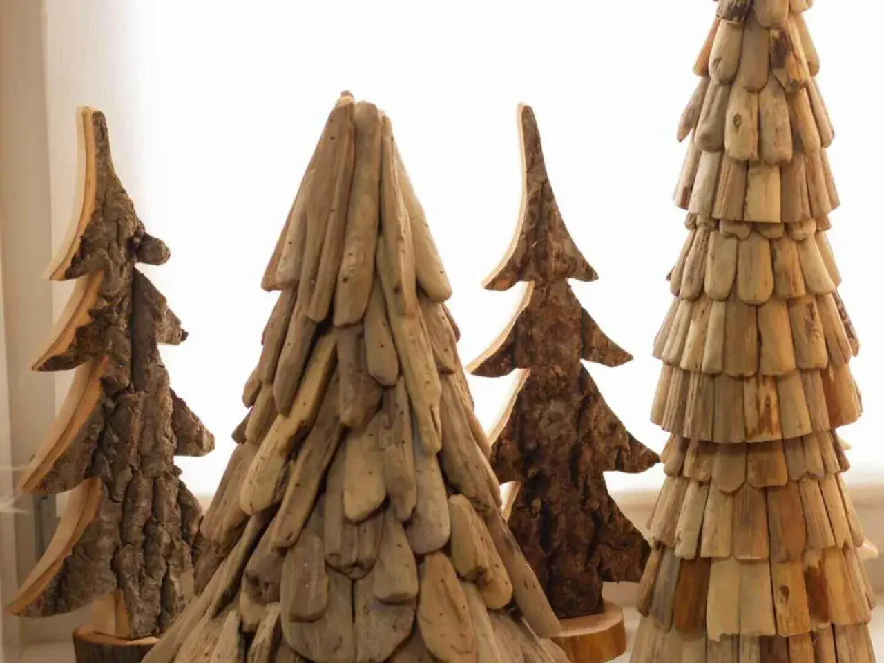 Rustikale Weihnachtsdeko Holz selber machen: Vier handgefertigte Bäume aus Holzstücken und Rinde, die an Tannen erinnern.