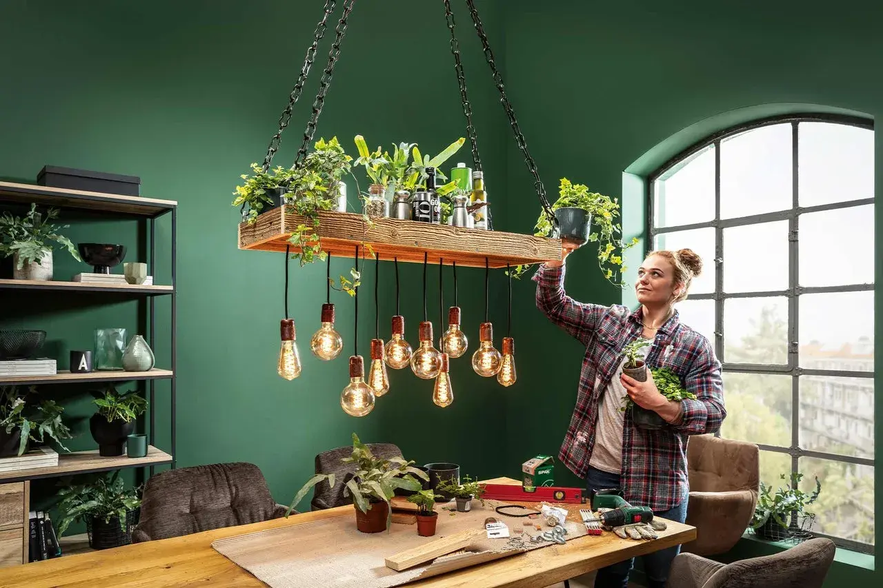 Frau dekoriert eine selbstgemachte Lampe mit Pflanzen. Ein DIY-Projekt für ein grünes Zuhause.