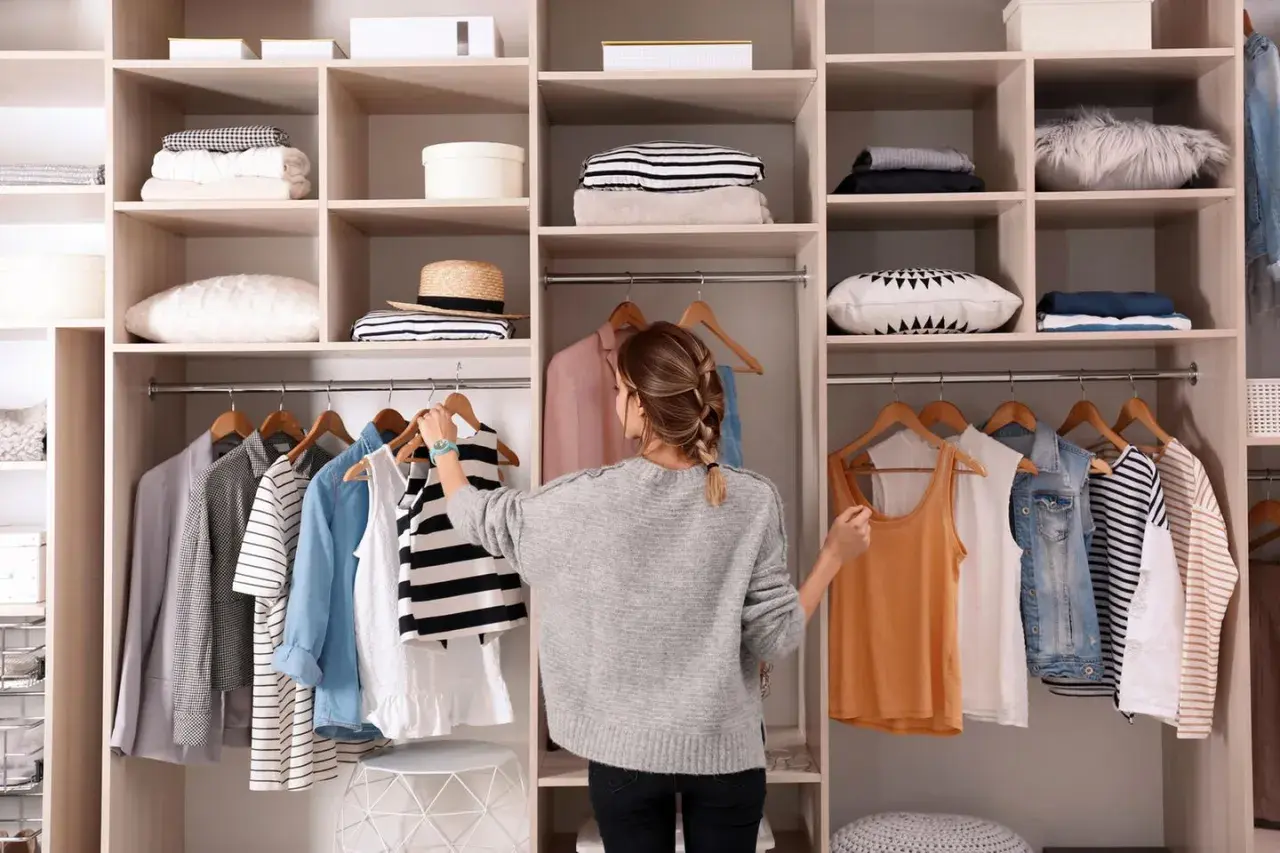 Frau sortiert Kleidung im offenen Kleiderschrank. Hier sind clevere Kleiderschrank Aufteilung Tipps für Ordnung.