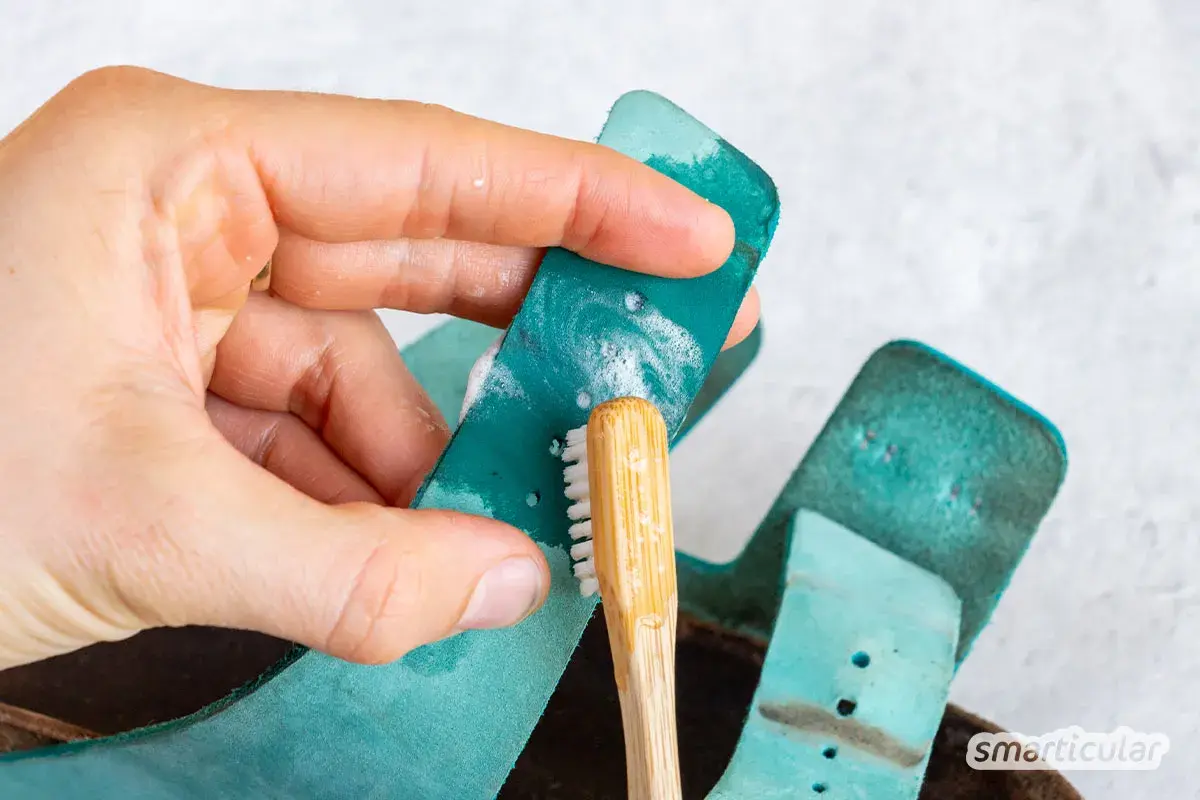 Hand reinigt türkisfarbene Birkenstock-Riemen mit einer kleinen Bürste und Seife. So einfach ist das Birkenstock reinigen!