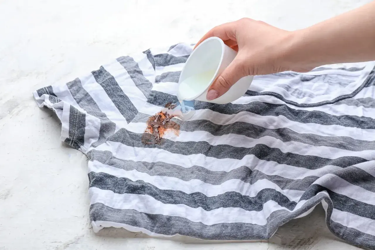 Flüssigkeit wird auf einen Fleck auf einem gestreiften T-Shirt gegossen, um Wandfarbe aus Kleidung zu entfernen.