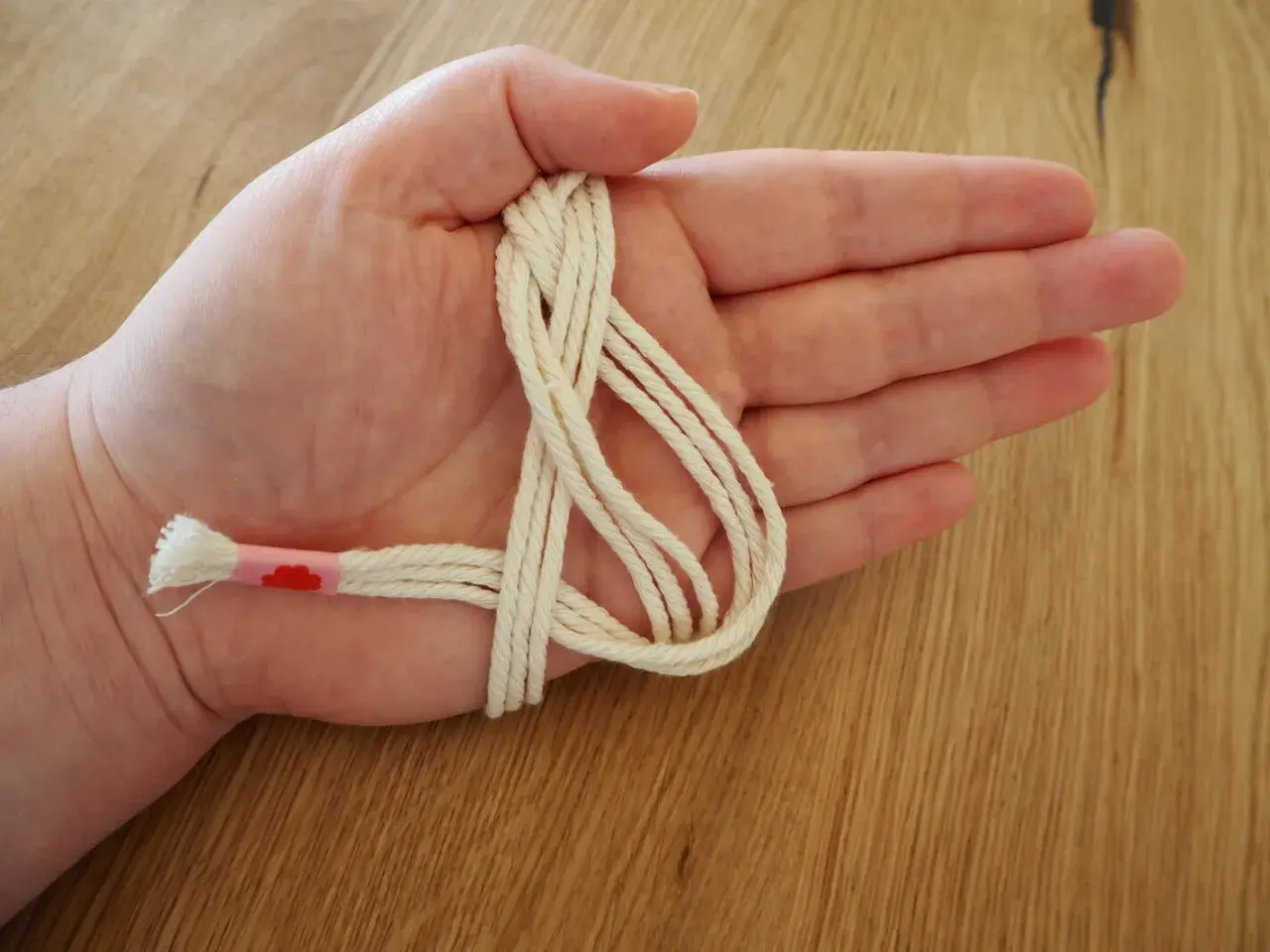 Hand hält cremefarbene Schnur für makramee serviettenringe anleitung. Ein Teil ist mit rosa Band umwickelt.