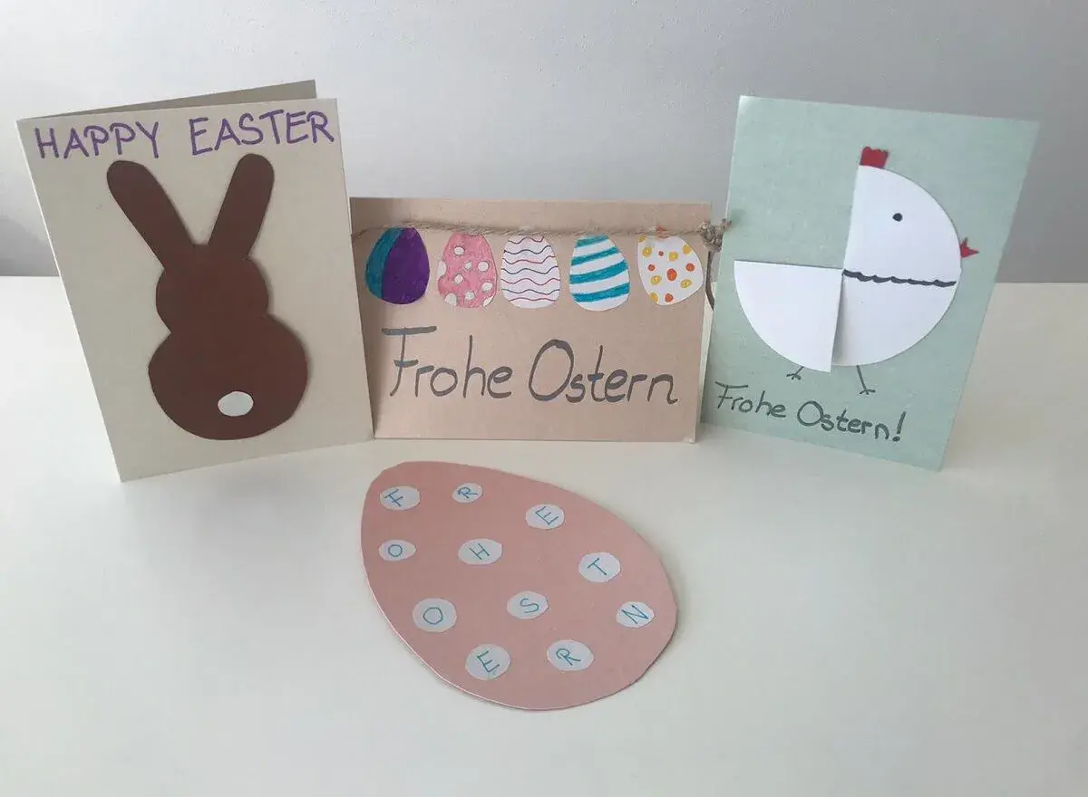 Osterkarten basteln einfach: Hase, Küken und bunte Eier. Ein rosa Ei mit Buchstaben für "Frohe Ostern" liegt vorne.