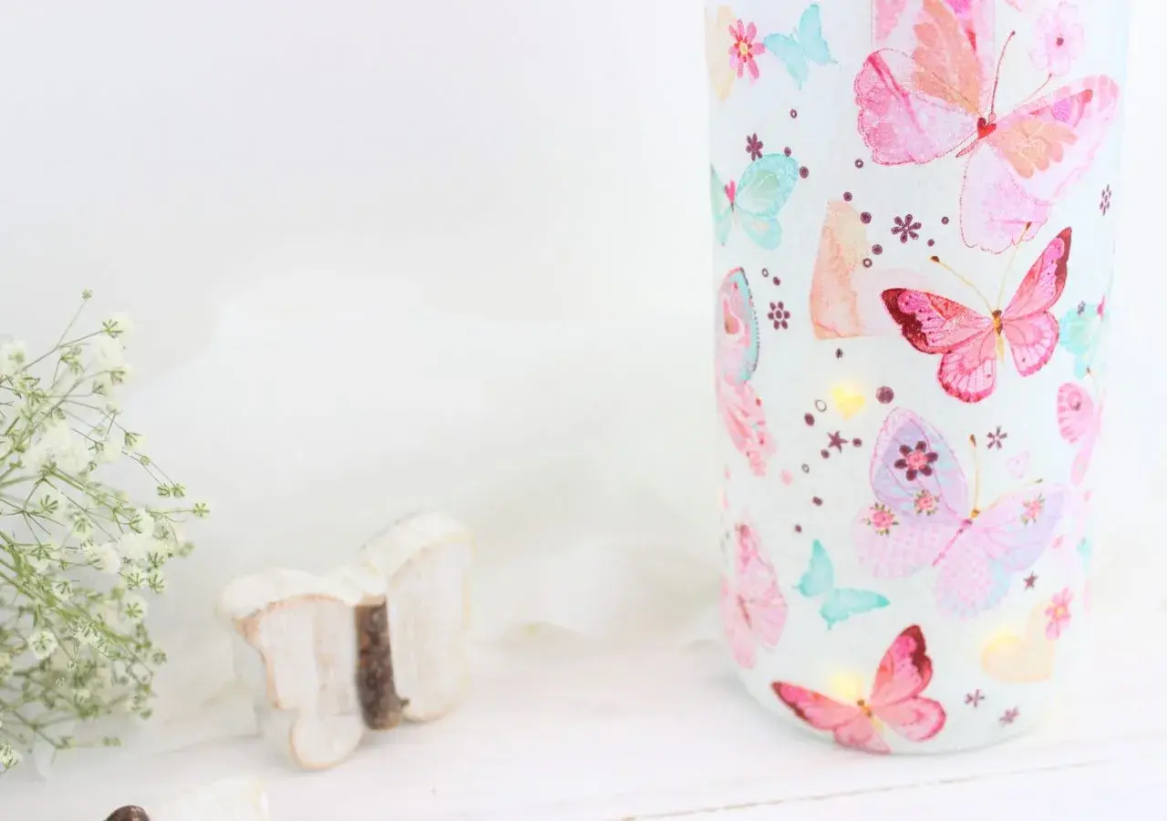 Zauberhaftes Basteln mit Servietten: Ein Glas mit bunten Schmetterlingen, kleine Lichter und eine Holzschmetterling-Deko.
