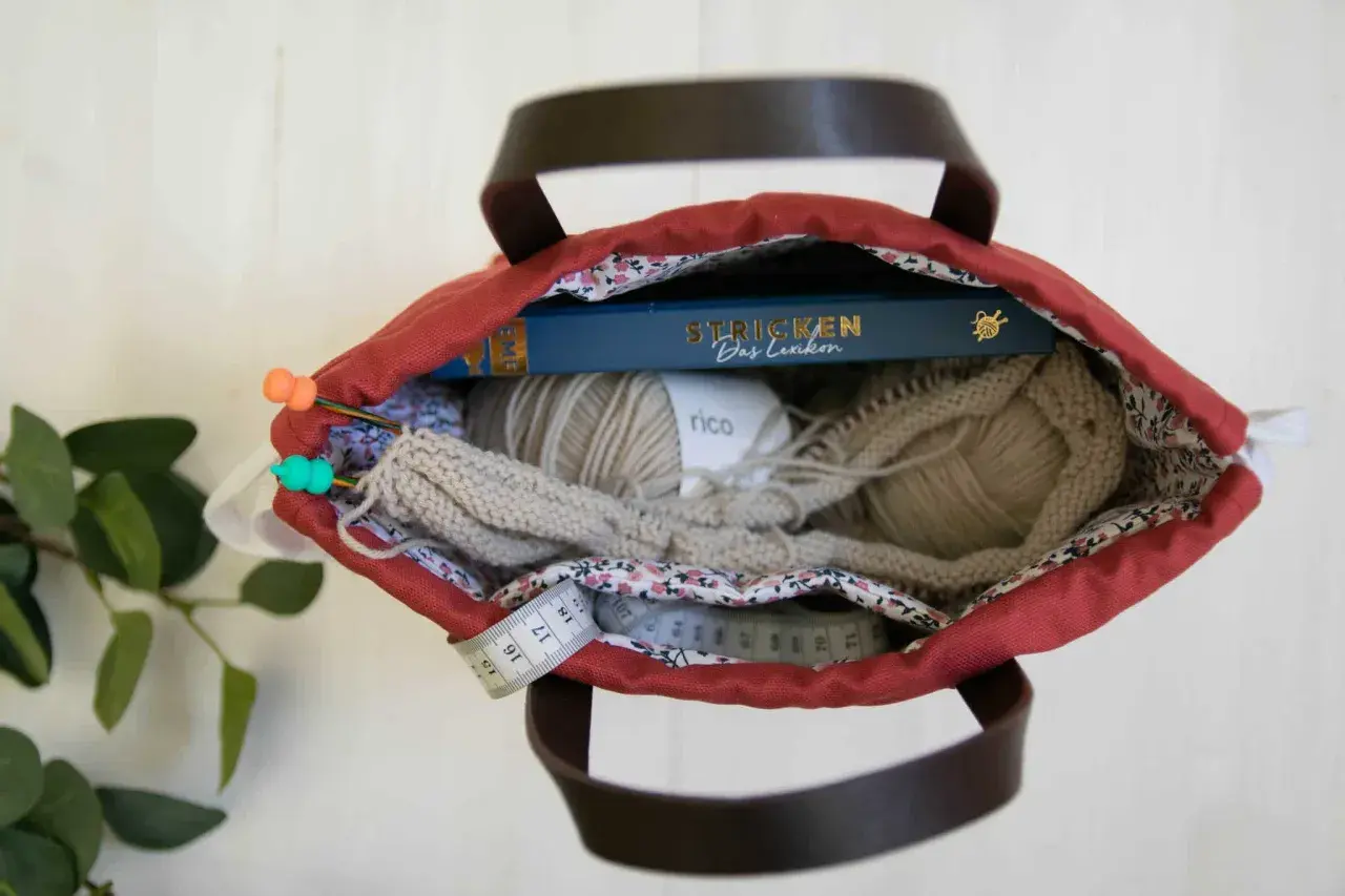 Kreative Ideen für upcycling taschen selber machen: Wolle, Stricknadeln, ein Buch und Maßband in einer roten Tasche.