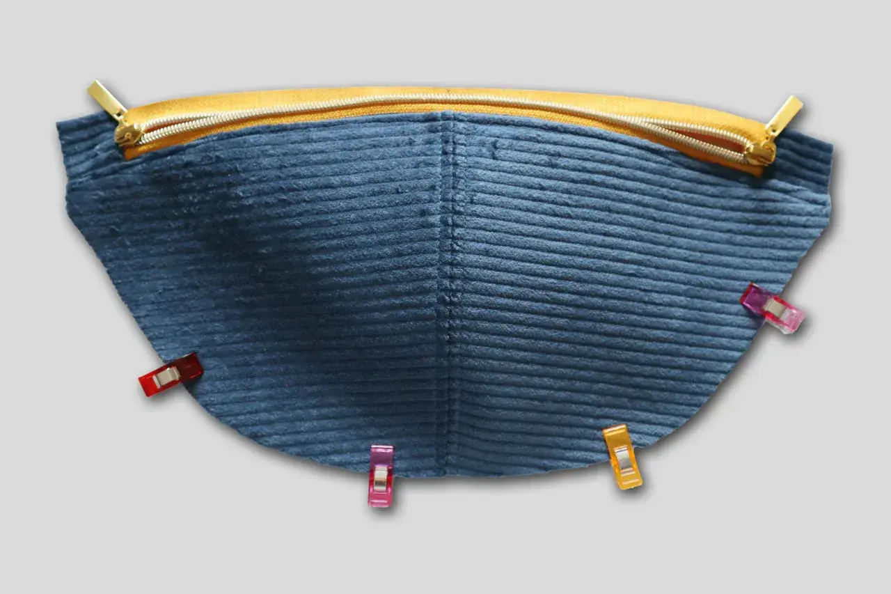 Blauer Cordstoff mit Reißverschluss und Nähklammern, bereit für das Schnittmuster einer Bauchtasche.