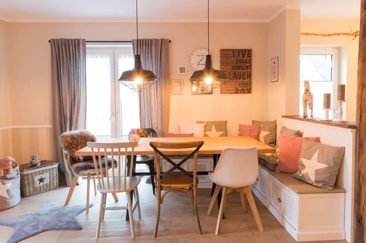 Gemütliches Esszimmer gestalten mit Holztisch, Bank und Stühlen. Dekorative Kissen und Wandbilder schaffen eine einladende Atmosphäre.