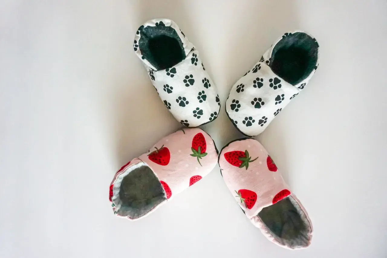 Zwei Paar süße Babyschuhe: eins mit Pfotenabdrücken, eins mit Erdbeeren. Hier findest du ein schnittmuster babyschuhe kostenlos zum Nachnähen!