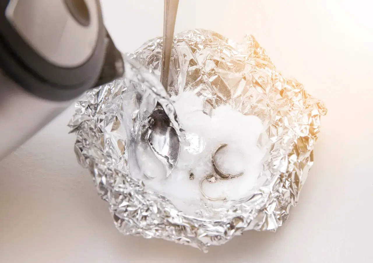 Silber putzen mit Natron: Heißes Wasser wird über Aluminiumfolie mit Natron und Schmuck gegossen, um angelaufenes Silber zu reinigen.