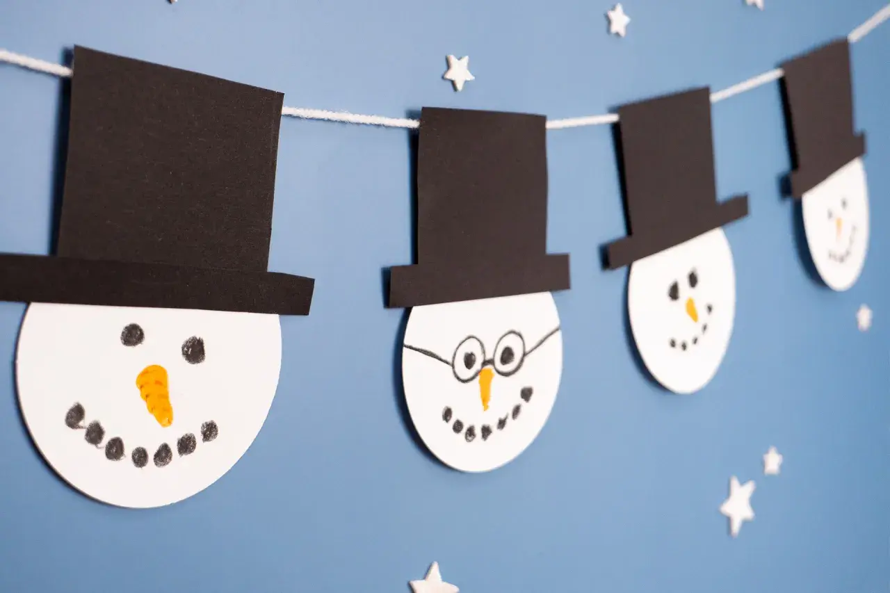Schneemann-Girlande als winter bastelideen kinder. Weiße Kreise mit schwarzen Hüten und Gesichtern hängen an einer Schnur.