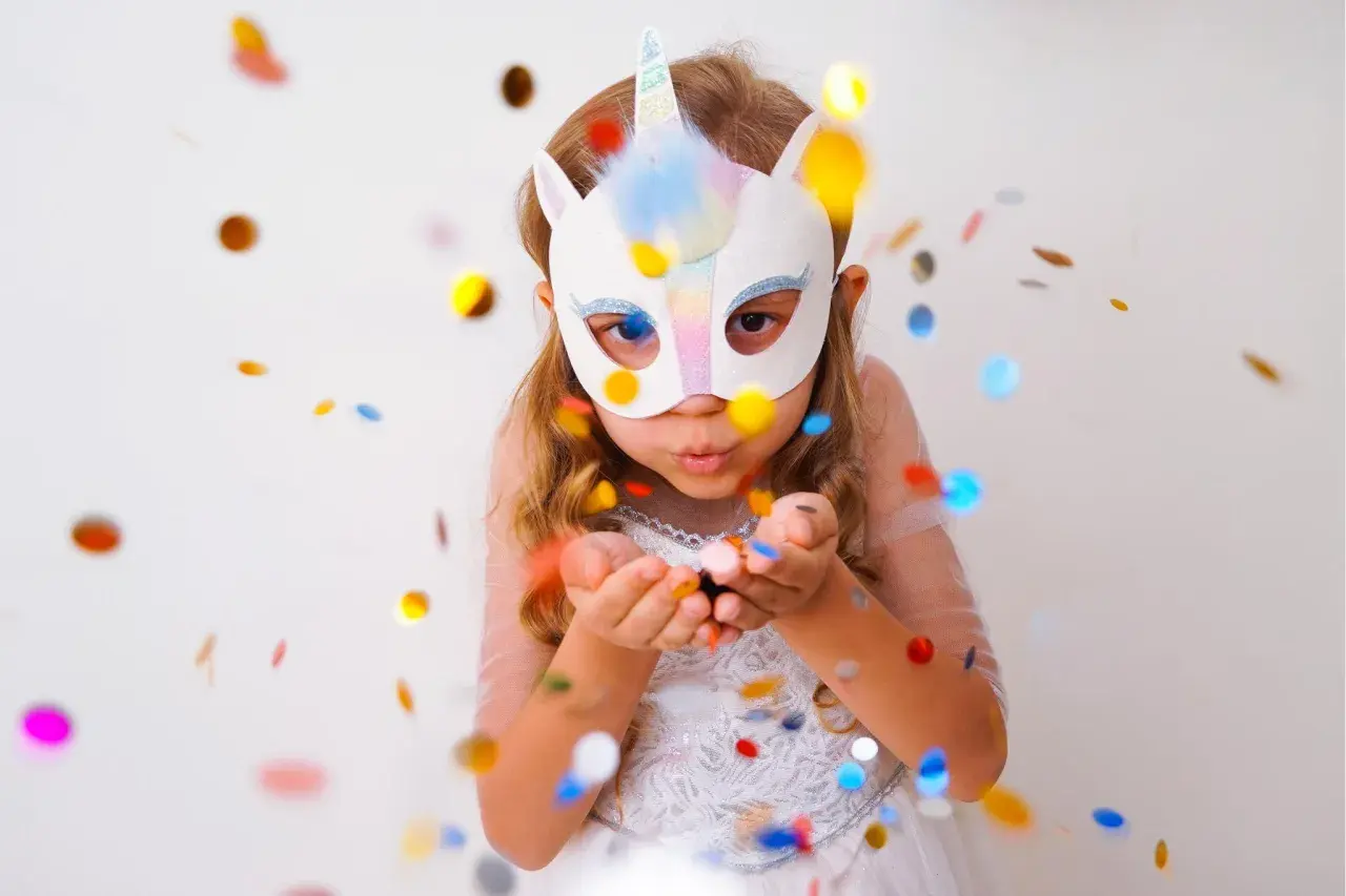 Ein Mädchen mit Einhorn-Faschingsmaske bläst Konfetti. Eine tolle Vorlage für deine nächste Party!