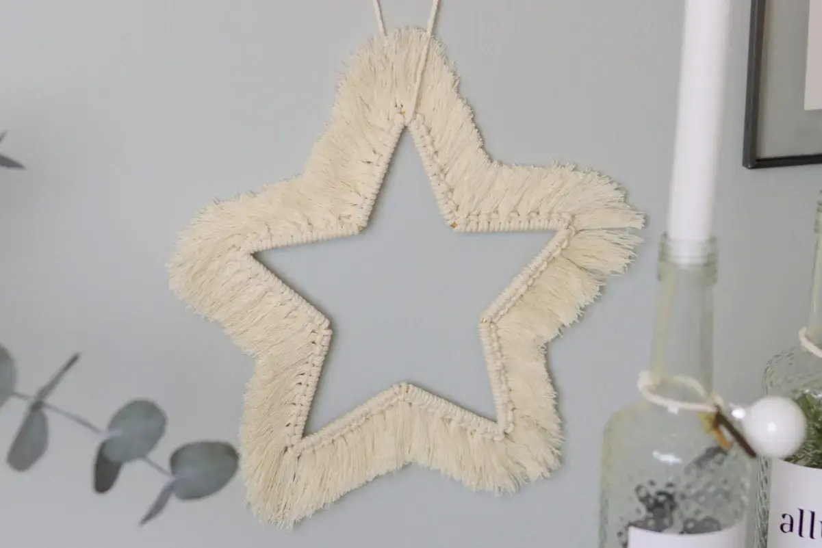 Ein Makramee Stern an der Wand, der wie eine Anleitung zum Nachbasteln aussieht.