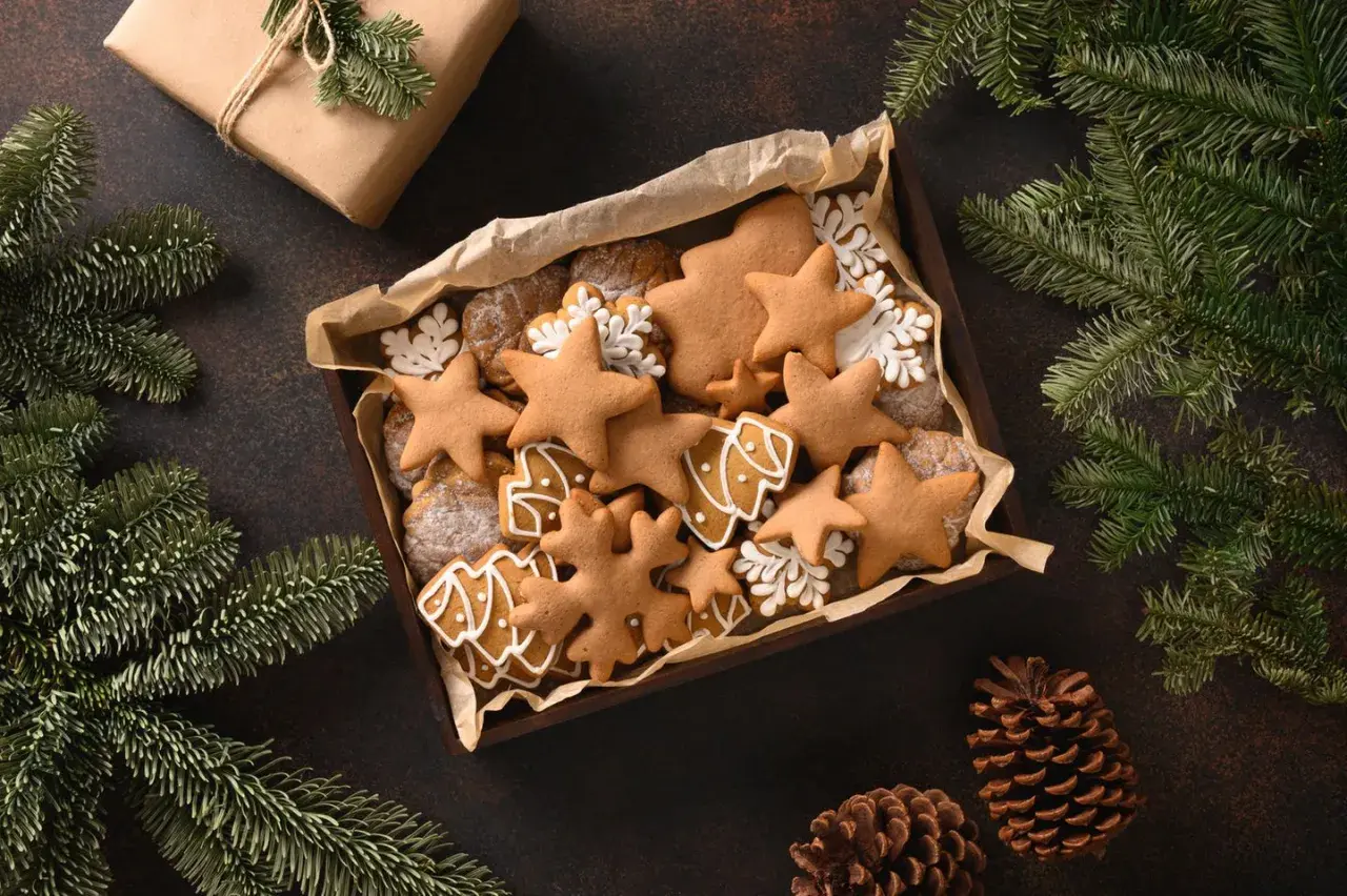 Kiste mit selbstgemachten Weihnachtsplätzchen, Sternen und Bäumen, perfekt zum Basteln von Weihnachtsgeschenken. Tannenzweige und Zapfen schmücken die Szene.