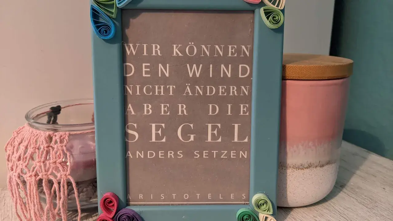 Ein hellblauer Bilderrahmen mit Quilling-Verzierungen, der ein Zitat von Aristoteles zeigt: "Wir können den Wind nicht ändern, aber die Segel anders setzen". Eine schöne alte Bilderrahmen Deko Idee.