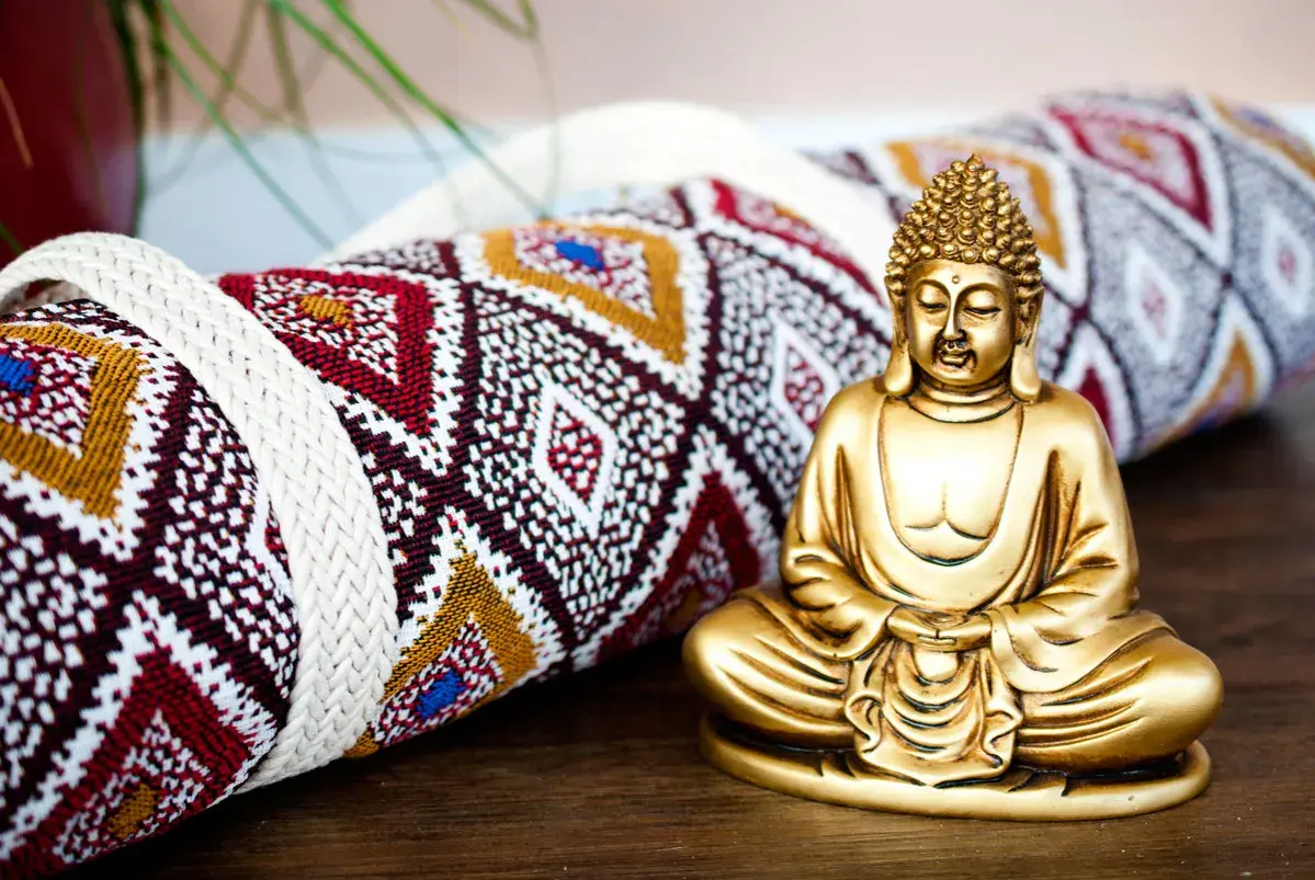Goldene Buddha-Figur neben einer gerollten Yogamatte mit ethnischem Muster. Vielleicht das Schnittmuster für eine Yogatasche?