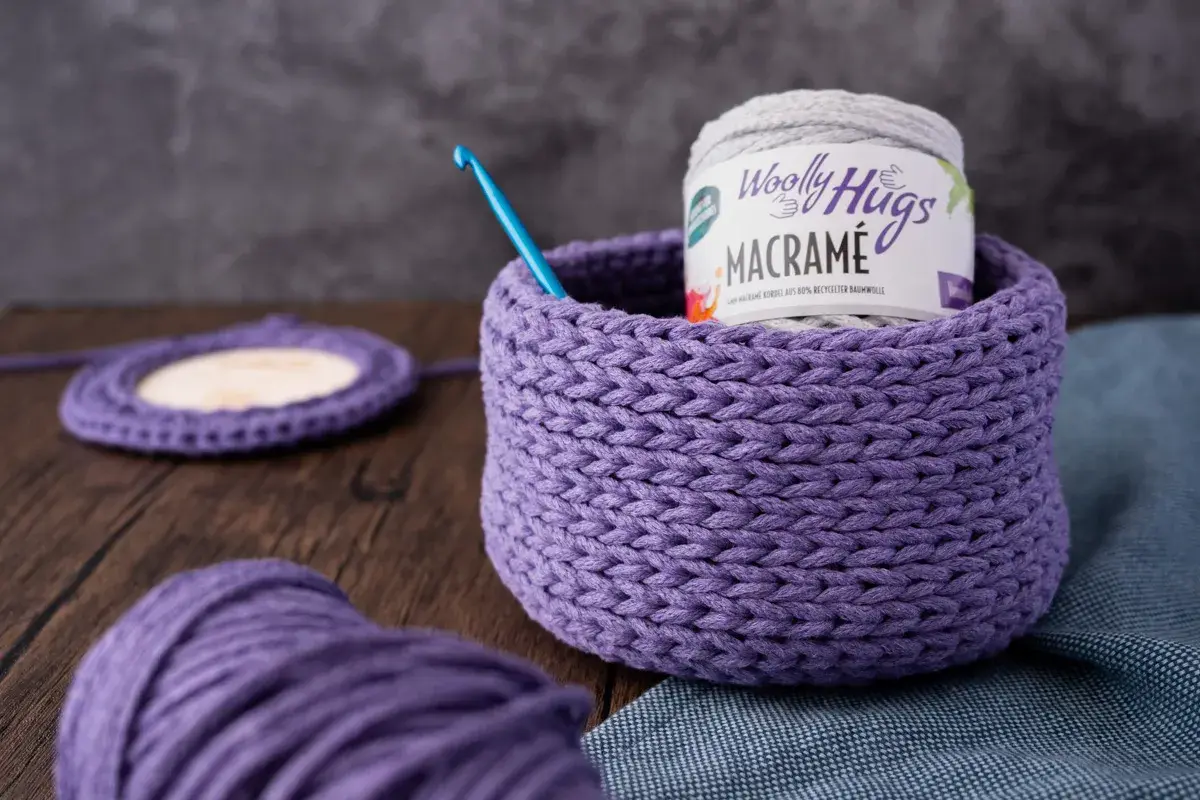 Ein lila gehäkelter Korb mit Garnrolle und Häkelnadel. Perfekt für eine makramee korb anleitung.