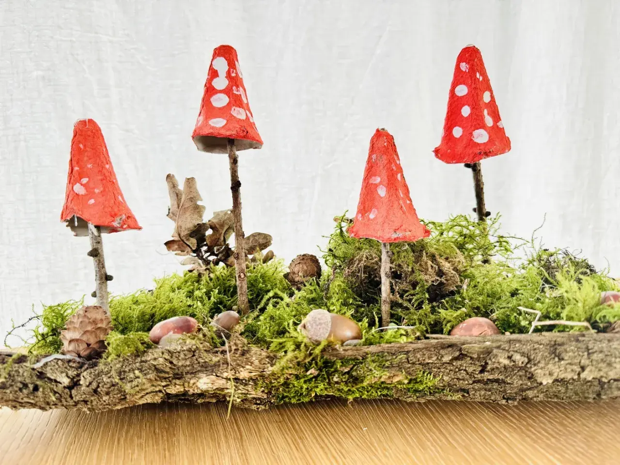 Zauberhafte herbstdeko diy: Fliegenpilze aus Eierkartons auf Moos und Baumrinde, dekoriert mit Zapfen und Kastanien.