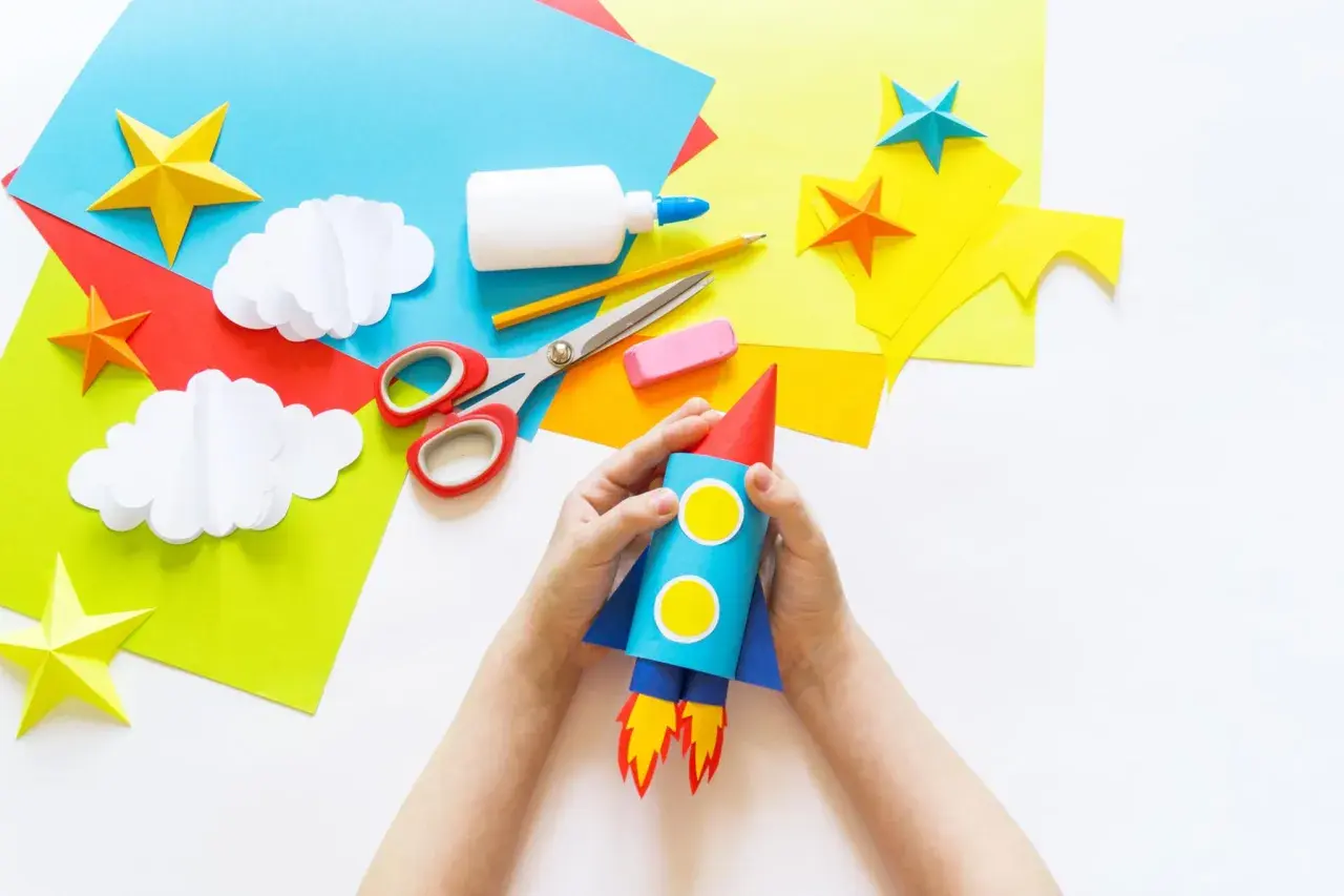 Kinder basteln einen Raketen-Weltraumflug. Alles für bastelkleber selber machen liegt bereit: Papier, Schere, Kleber, Stift.