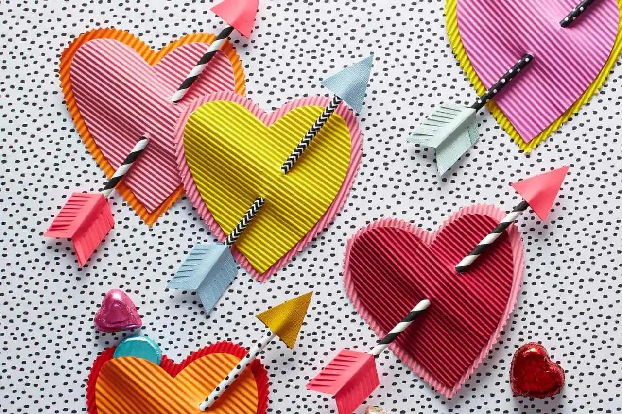 Bunte Herzen mit Pfeilen, perfekt zum Basteln zum Valentinstag. Kleine Schokoladenherzen liegen daneben.