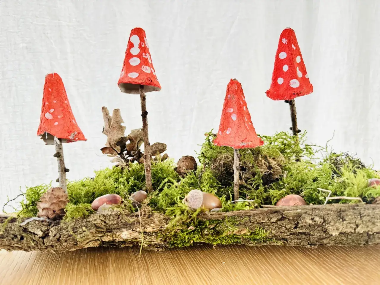 Zauberhafte herbstdeko diy: Fliegenpilze aus Eierkartons auf Moos und Rinde, verziert mit Zapfen und Kastanien.